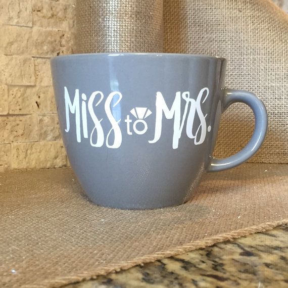 a gray coffee cup sitting on top of a counter next to a brick wall with the word miss and mrs written in white