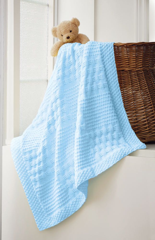 a teddy bear sitting on top of a basket next to a blue knitted blanket