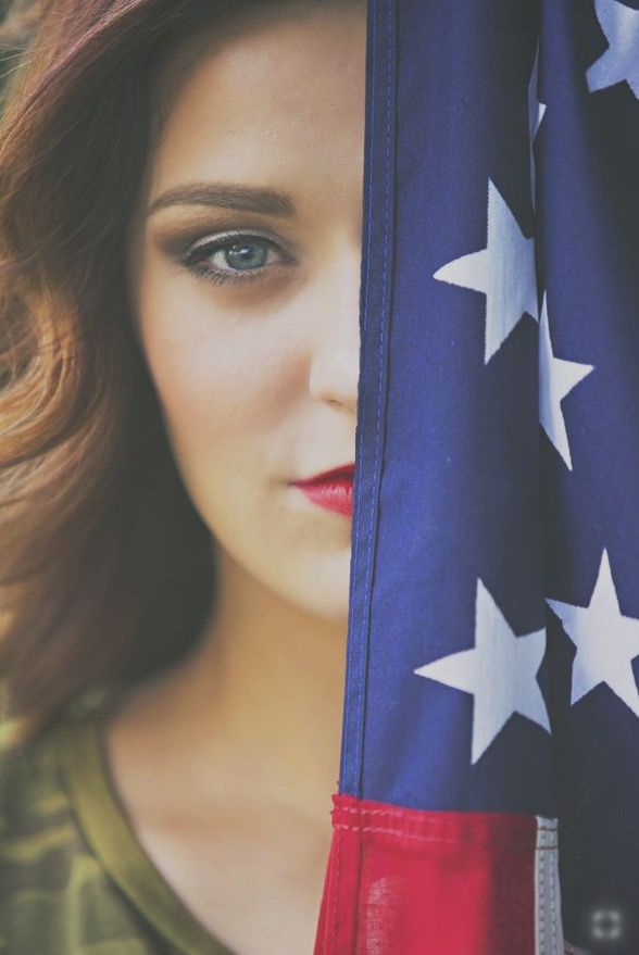 a beautiful young woman holding an american flag in front of her face and looking at the camera