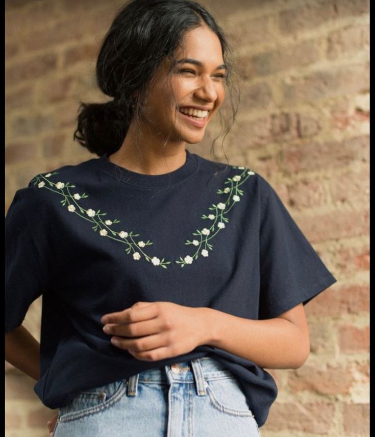 a woman standing in front of a brick wall wearing a t - shirt with flowers on it