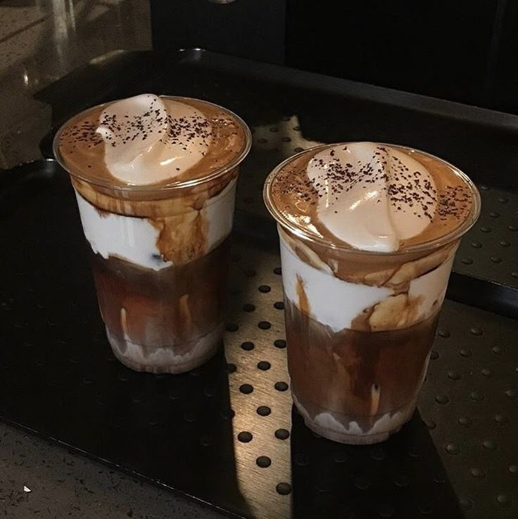 two glasses of iced coffee sitting on top of a black table next to each other