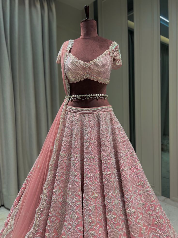 Reverie Bridal set is a stunning coral pink lehenga hand embroidered on pure raw silk fabric with signature glass crystals, pearls, sequins, and beads and has scalloped edges on the lehenga. It's paired with an attractive hand-embroidered blouse with cap sleeves on net fabric. It comes with a peachy pink soft net scalloped dupatta, a gorgeous soft net trail dupatta, and a pearl belt that enhances the entire look.From Rianta's Naayab collection. DELIVERY TIMEPlease allow 8-12 weeks for your outfi Bridal Lehanga Blouses Modern Design, Pink Lehenga For Bride, Mera Aesthetic, Modern Lehangas, Trending Bridal Lehenga, Trending Lehenga Designs, Swiss Vacation, Scalloped Dupatta, Lehenga Pink