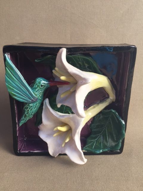 a white flower and green leaves on a purple plate with a bird figurine