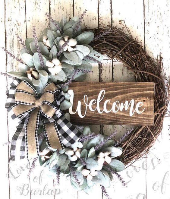 a wooden sign that says welcome with flowers and leaves on it, sitting next to a wreath