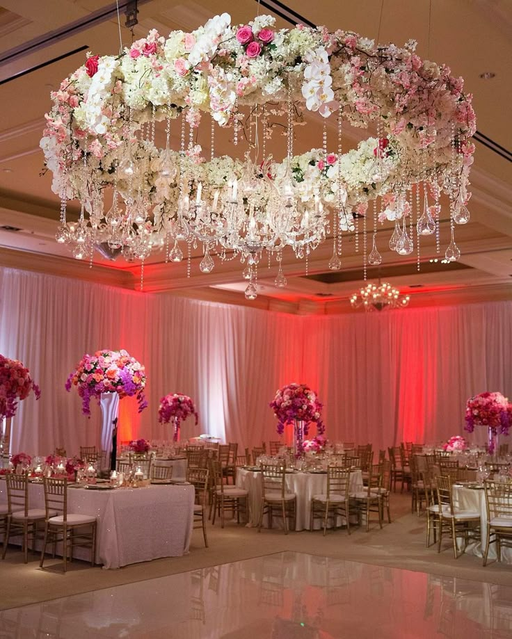 an elegant wedding setup with chandeliers and flowers on the ceiling, along with tall centerpieces