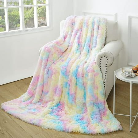 a white couch sitting next to a window covered in a rainbow colored fluffy throw blanket