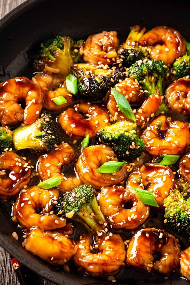 a skillet filled with shrimp and broccoli on top of a wooden table