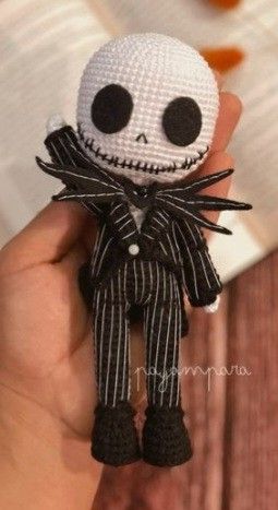 a hand holding a small crocheted jack skellingy doll with black and white stripes