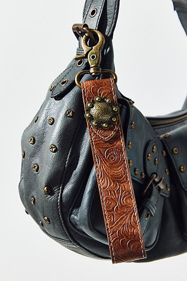 a black purse with brown leather handles and studded details on the front, hanging from a hook