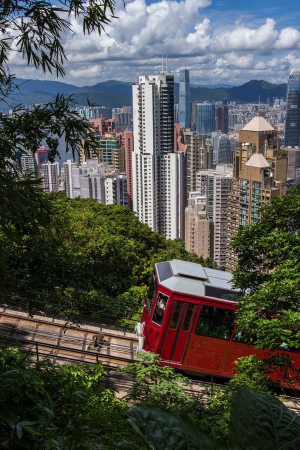 a red and white train traveling through a lush green forest covered hillside next to tall buildings