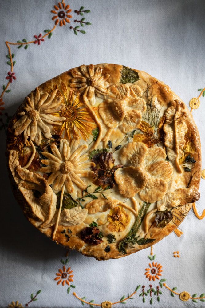 an elaborately decorated pie sitting on top of a white tablecloth covered in flowers