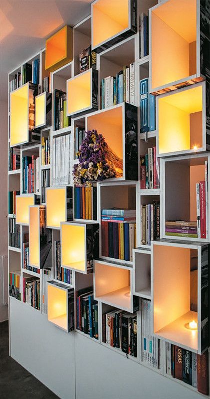 a bookshelf filled with lots of books next to a wall covered in lights