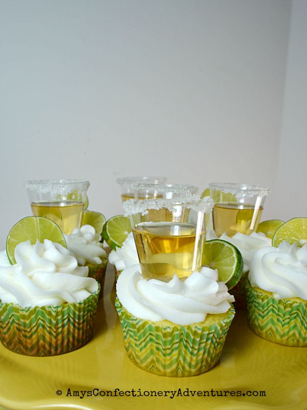 cupcakes with white frosting and lime slices on a yellow plate next to cups