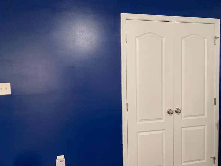 a blue room with two white doors and a light switch on the wall next to it