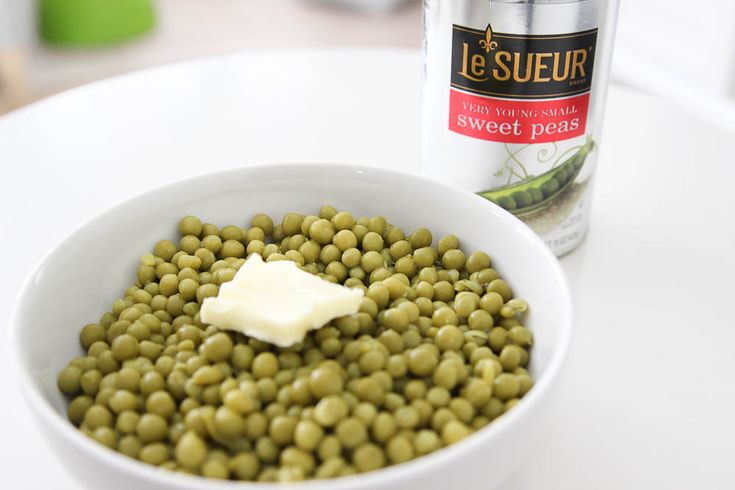 a white bowl filled with green peas next to a can of jesuefur