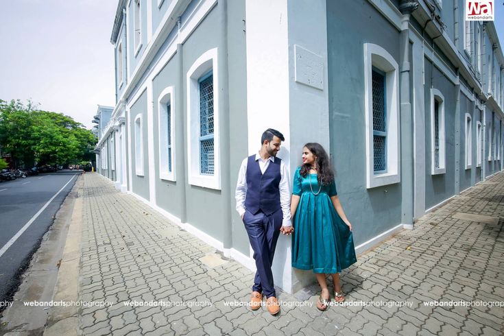 a man and woman standing next to each other in front of a blue building with white windows