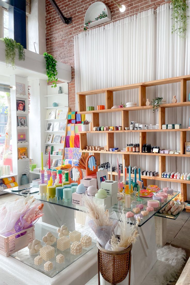 The interior of a boutique shop. In the foreground is a glass table with an assortment of candles of different shapes, sizes, and colors. Behind is a wall of shelves holding apothecary items, and to the left is a slim shelf holding books. Highland Park Los Angeles, Ceramic Store, Home Goods Store, Salon Suites, Concept Shop, Candle Store, Ceramic Shop, Handmade Boutique, Store Displays