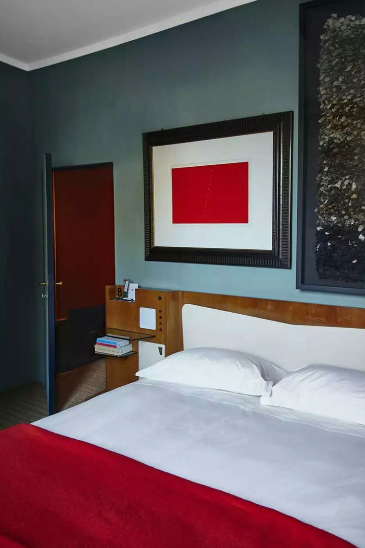 a bed with white sheets and red blanket in a blue room next to a painting on the wall