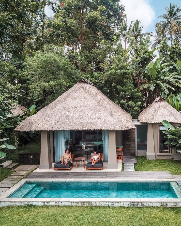 two people sitting on chairs in front of a swimming pool with thatched roof huts