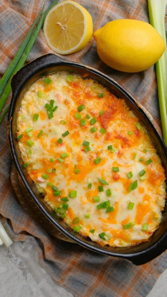 a casserole with cheese and green onions in a black pan next to lemons