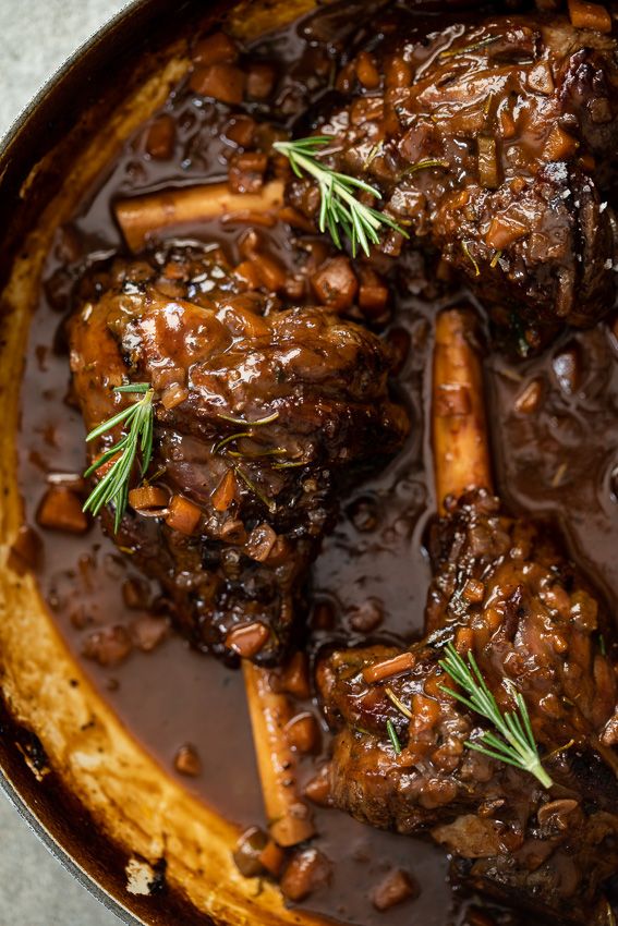 a pot filled with meat covered in gravy and garnished with rosemary