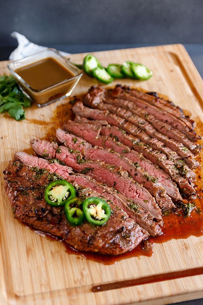 sliced steak with peppers and sauce on cutting board