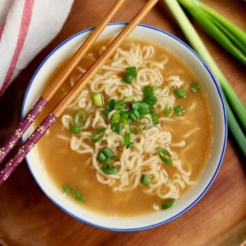 two chopsticks on top of a bowl of soup with noodles and green onions