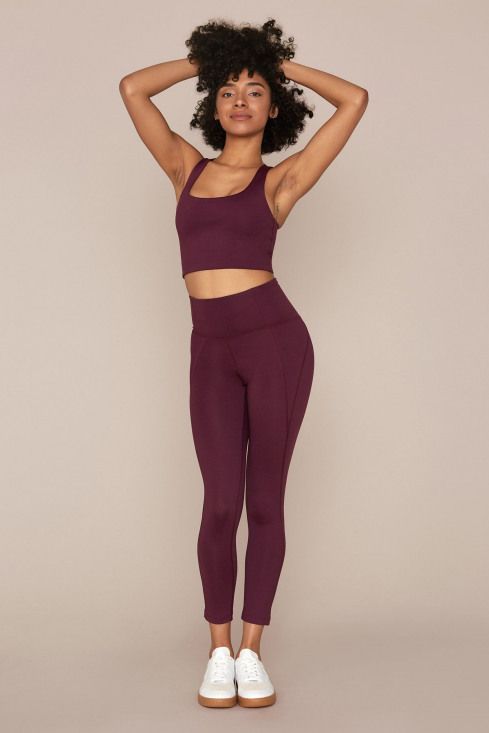 a woman in purple sports bra top and leggings with her hands on her head