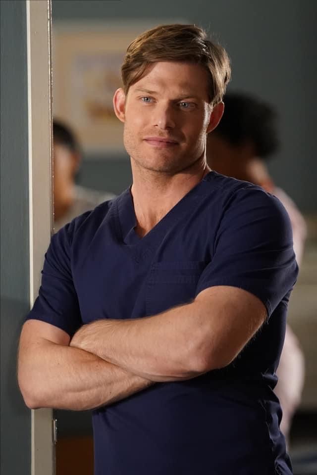 a man in scrubs leaning against a wall with his arms crossed and looking at the camera