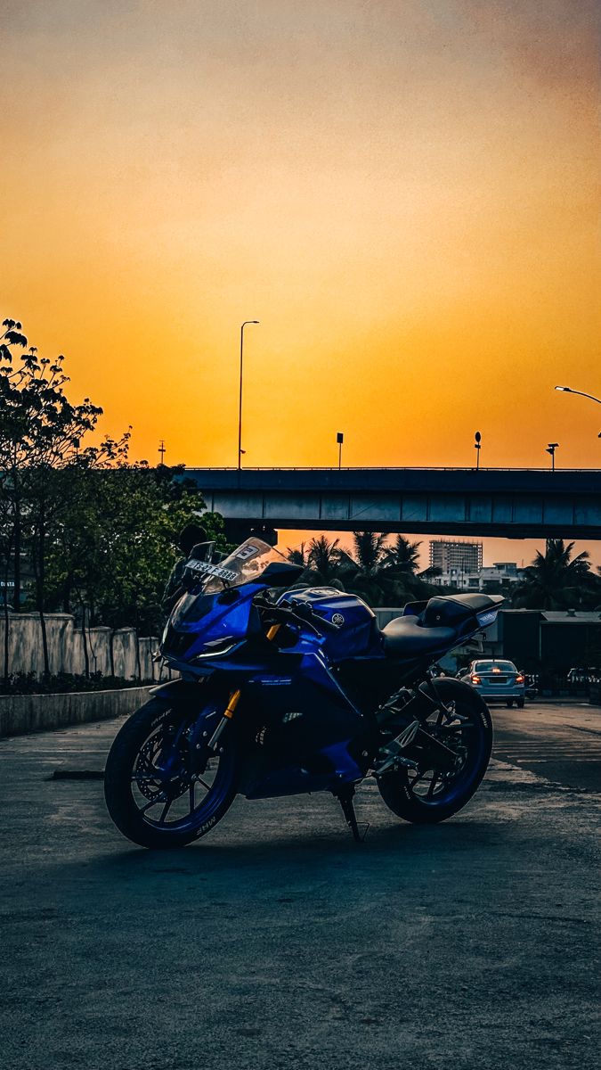 a blue motorcycle is parked in the parking lot at sunset or dawn with an overpass behind it