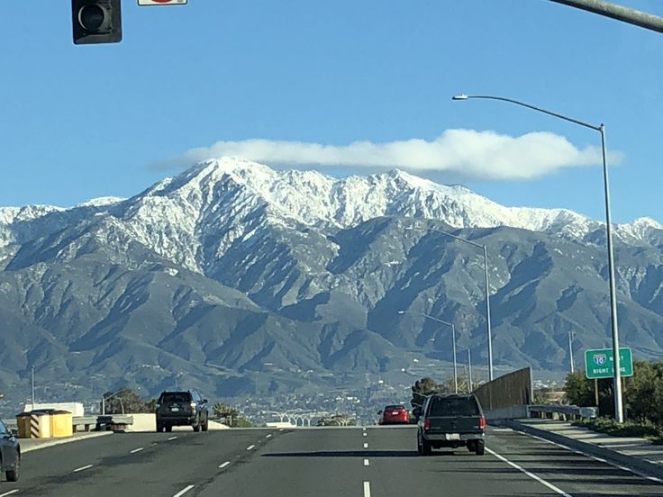 the mountains are covered in snow as cars drive down the road near traffic lights and street signs