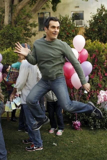 a man is dancing in the grass with balloons and flowers behind him as people look on