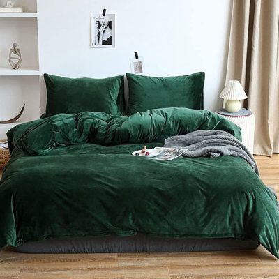 a bed with green comforter and pillows in a room next to a plant on the floor