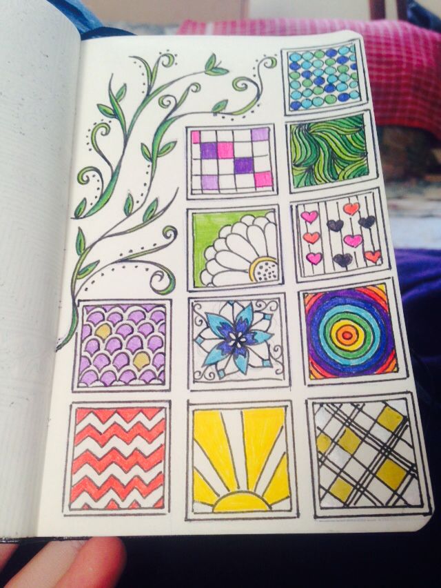 a hand holding an open coloring book with designs on it