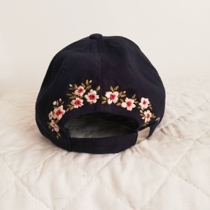 a black baseball cap with red and white flowers embroidered on the front, sitting on a bed