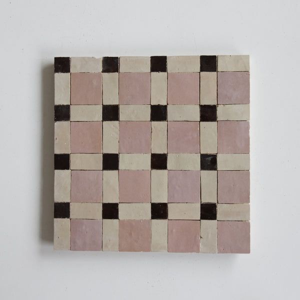 a square shaped tile with black and pink squares on the bottom, against a white wall