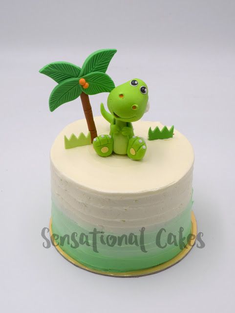 a small cake with a green dinosaur on top and a palm tree in the middle