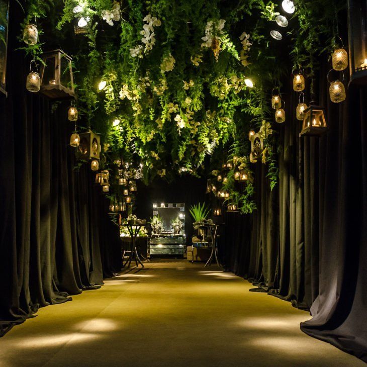 an outdoor area with lights and greenery on the ceiling, surrounded by black drapes