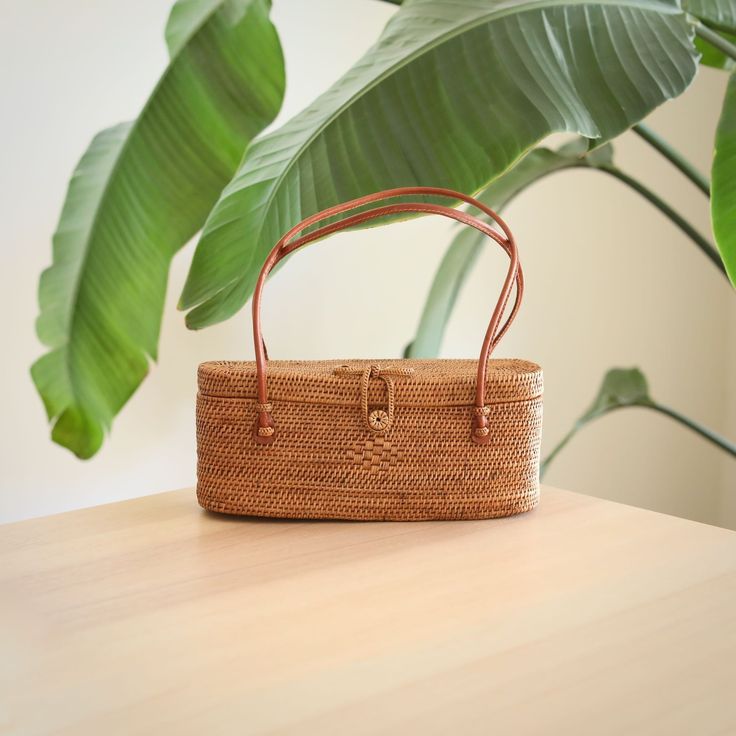 Underarm Bali Rattan Bag handmade by Ganapati Crafts in Bali sitting on a wood table looking amazing for stylish women Eco-friendly Rattan Bag For Daily Use, Eco-friendly Natural Rattan Bag, Grass Weaving, Eco-friendly Rattan Straw Bag With Bamboo Handle, Eco-friendly Woven Rattan Crochet Bag, Eco-friendly Rattan Shoulder Bag With Open Weave, Rattan Bag, Well Woven, Elevate Your Look