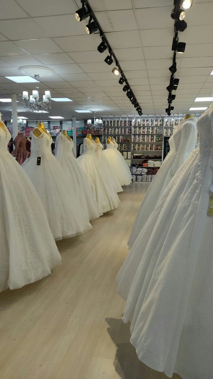 wedding gowns are on display in the aisle of a store, with lights hanging from the ceiling