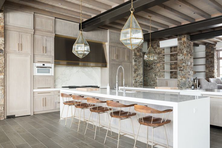 a large kitchen with an island and bar stools in the center, surrounded by stone walls