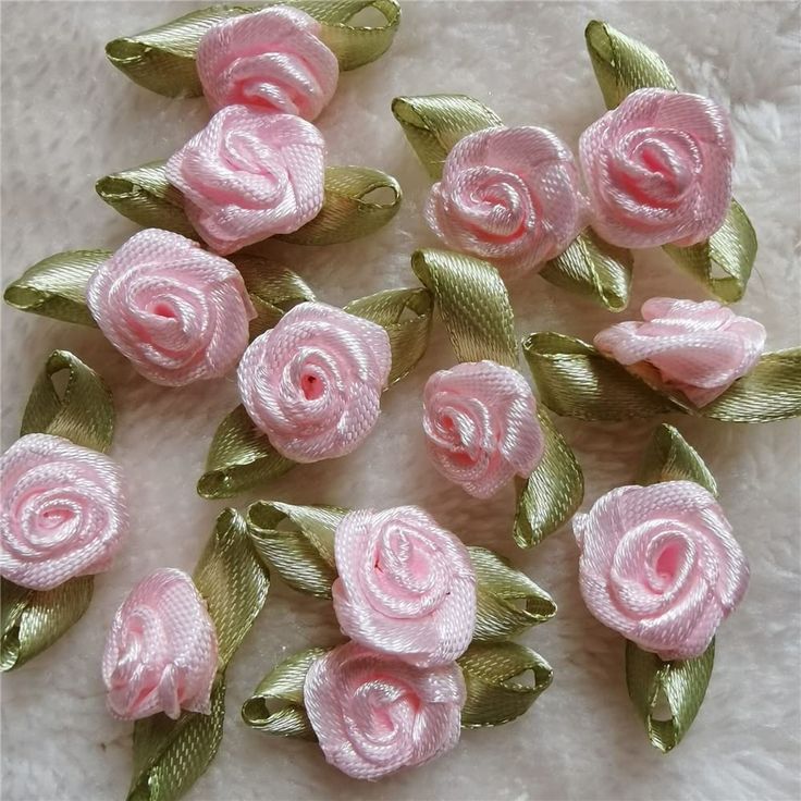 several pink roses with green leaves on a white surface and some are made out of fabric