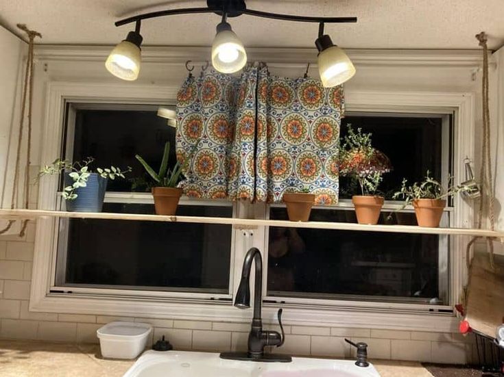 a kitchen window with potted plants on the ledge and lights hanging from the ceiling