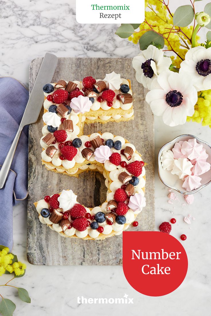 the number 5 cake is decorated with fresh berries and flowers on a cutting board next to a knife