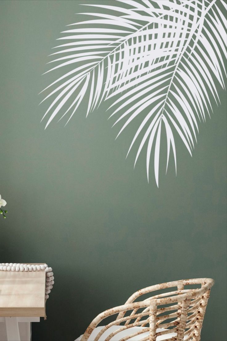 a palm leaf wall decal on a green wall next to a wicker chair