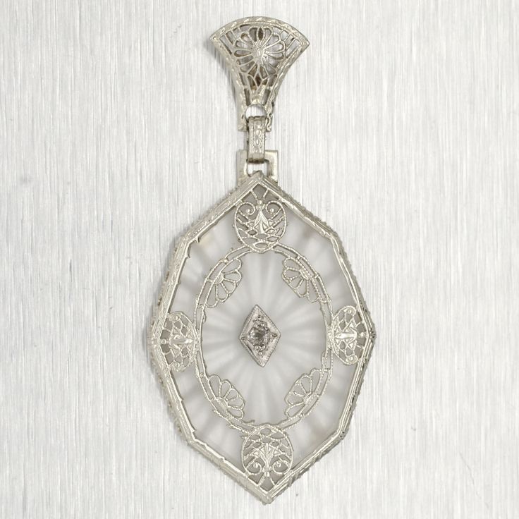 Design:This gorgeous pendant is an elongated octagon shape, adorned with lacey white gold accents on the front. The transparent center that allows the back's sunburst pattern to shine without distracting from the focal diamond. Diamond Details -  Color: G -  Clarity: I1 -  Carat Weight Total:  0.01ct approximately -  Stone Cut Shape: Round Cut Pendant Measurements:31.00 x 21.00 x 3.80 mm Inner Bail Measurements:5.37 x 2.88 mm Drop Length:46.56 mm Total Weight:5.0 grams Composition:This item has Octagon-shaped Single Cut Diamond Platinum Jewelry, Victorian White Jewelry With Single-cut Diamonds, Platinum Octagon Jewelry With Single Cut Diamonds, Victorian White Jewelry With Single Cut Diamonds, Victorian Style White Jewelry With Single Cut Diamonds, Victorian White Platinum Jewelry, Silver Octagon Engraved Jewelry, Elegant White Octagon Necklace, Antique White Diamond Cut Jewelry