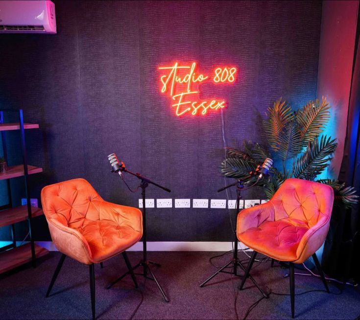 two orange chairs sitting next to each other in front of a neon sign