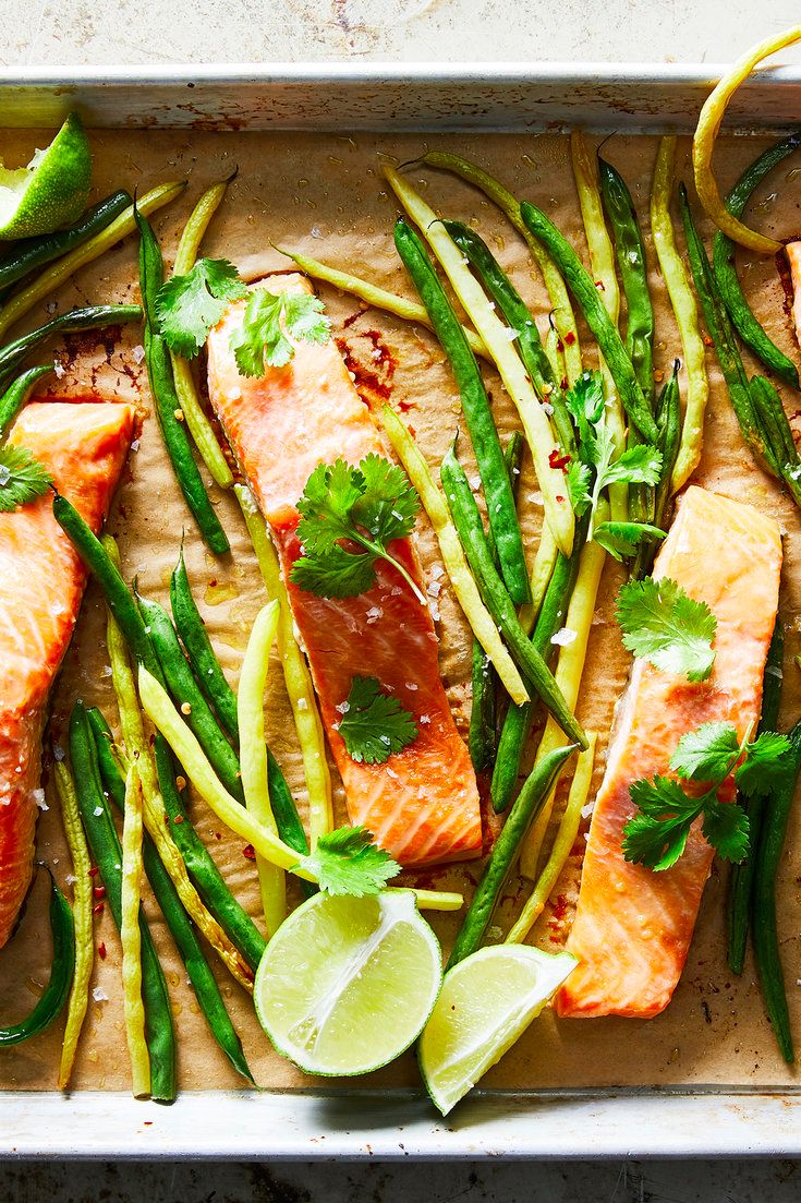 salmon and asparagus on a baking sheet with lemon wedges, cilantro