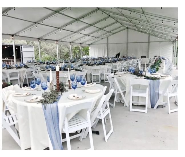 tables and chairs are set up in a tent for an outdoor event with white tablecloths and blue vases