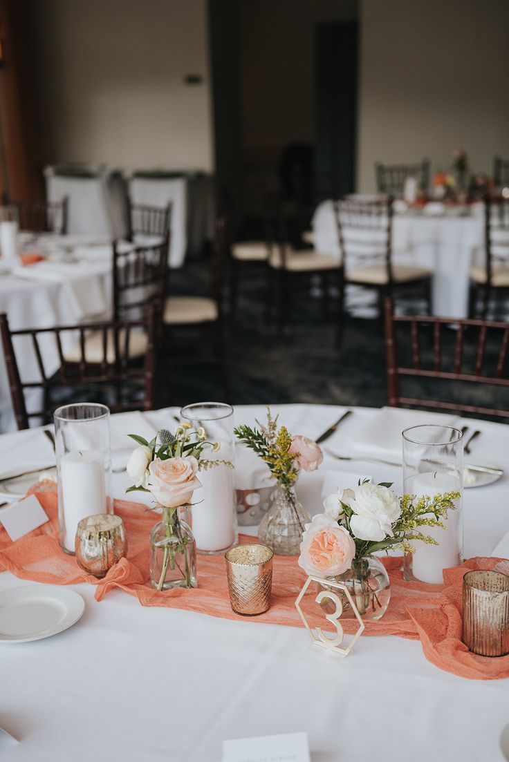 the table is set with white and pink flowers in vases, candles, and napkins